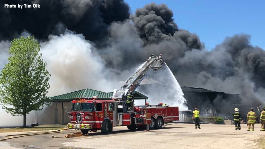 Tower ladder flows water on burning building as black smoke rears up