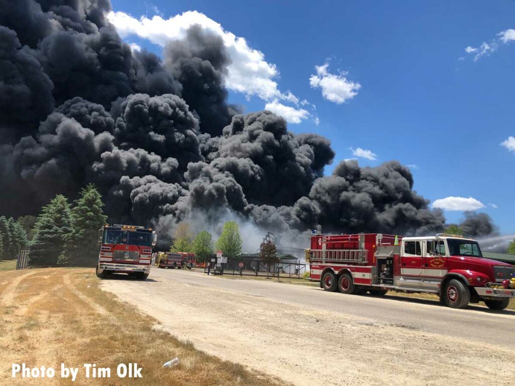 Gigantic plumes of smoke drift through sky past fire trucks