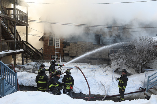 With the ladder still deployed, crews go defensive on the fire from an adjacent lawn.