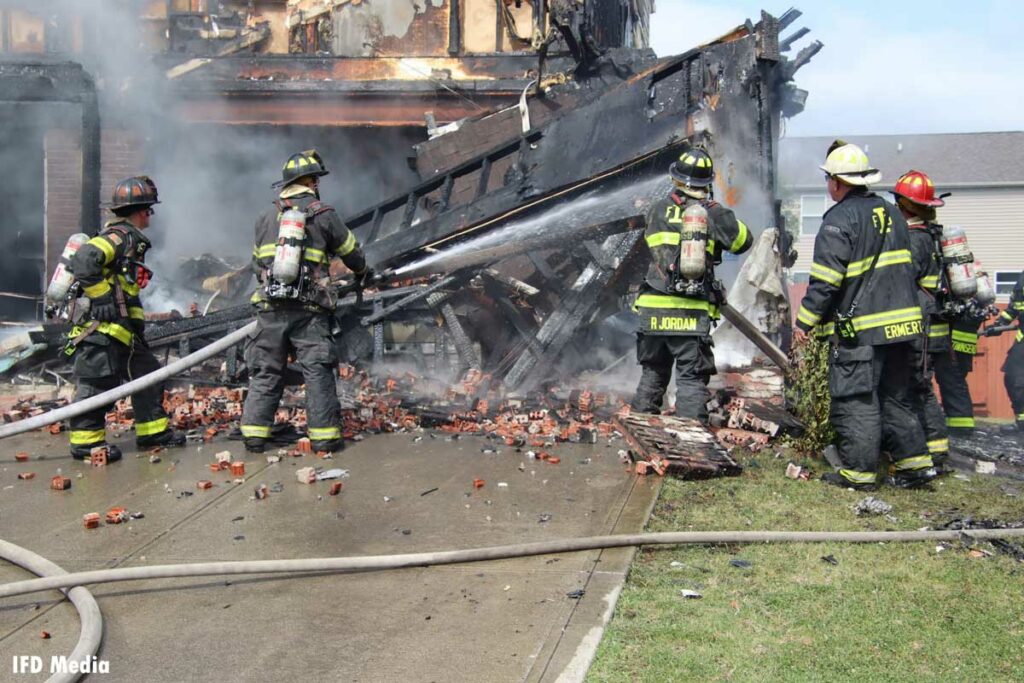 Firefighters put water on a charred, collapsed garage