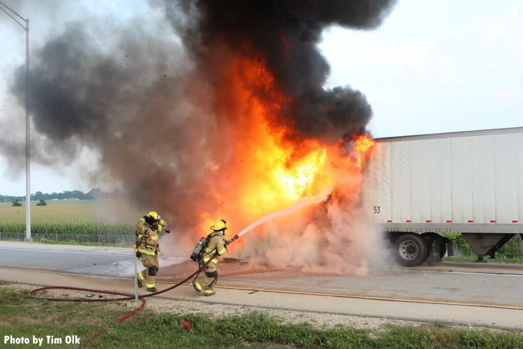 Flames erupt during a semi trailer fire in Illinois as firefighters manipulate a hoseline