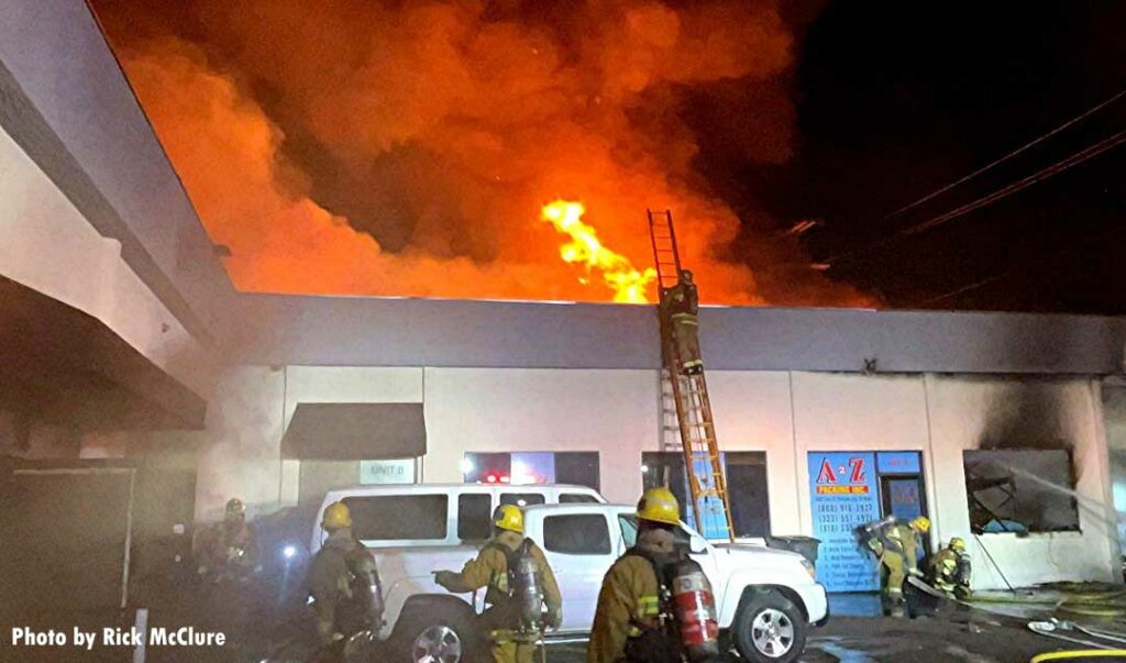 LAFD firefighter on a ladder with fire coming through the roof