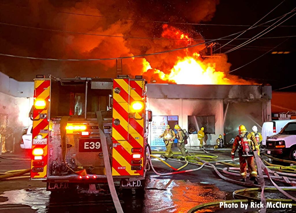 LAFD fire engine with hose flaked out everywhere and fire shooting from a building's roof