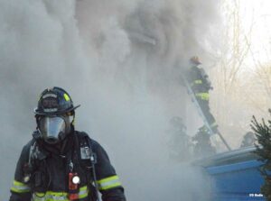 Indianapolis firefighter in full gear with firefighter on a ladder in the background partly obscured by smoke