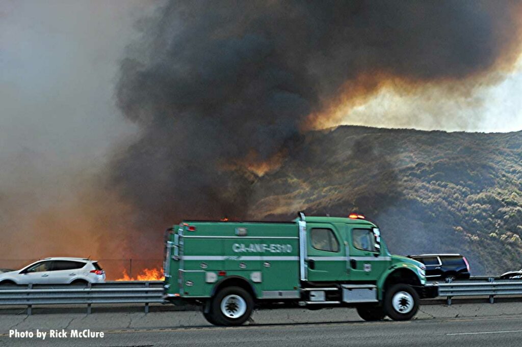 Fire burns on side of California roadway as traffic whizzes by