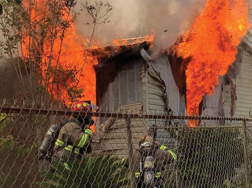 Firefighters with flames shooting through windows of structure