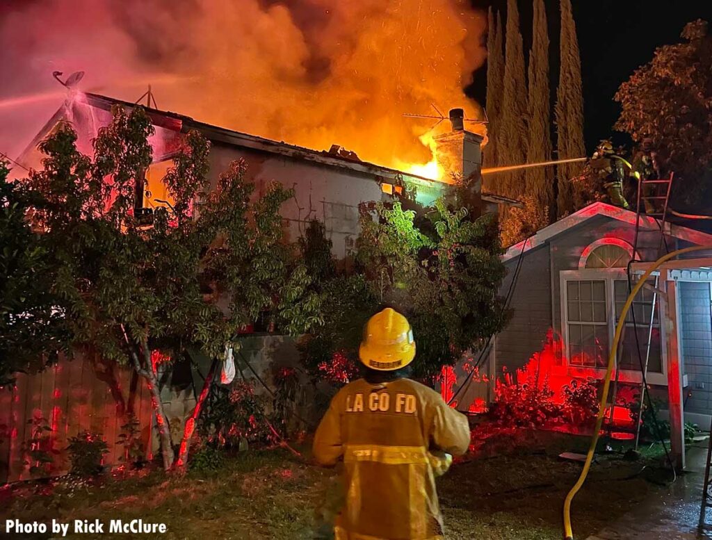 Firefighter trains hose stream on fire shooting from roof