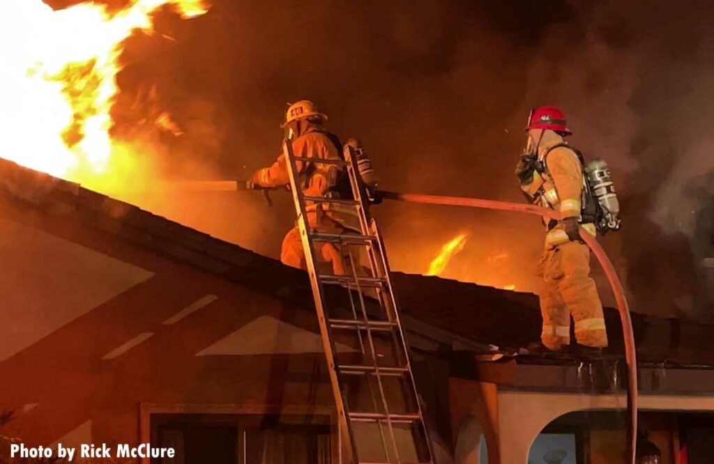 Firefighter trains hoseline on flames shooting through roof