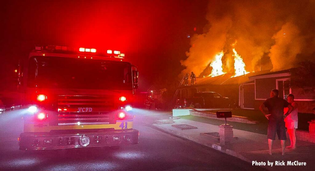 Fire truck with flames coming through roof at house fire