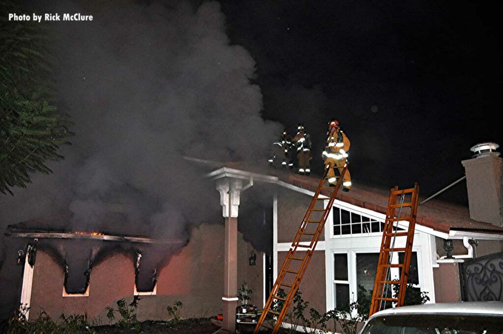 Two ladders and firefighters on the roof with smoke showing