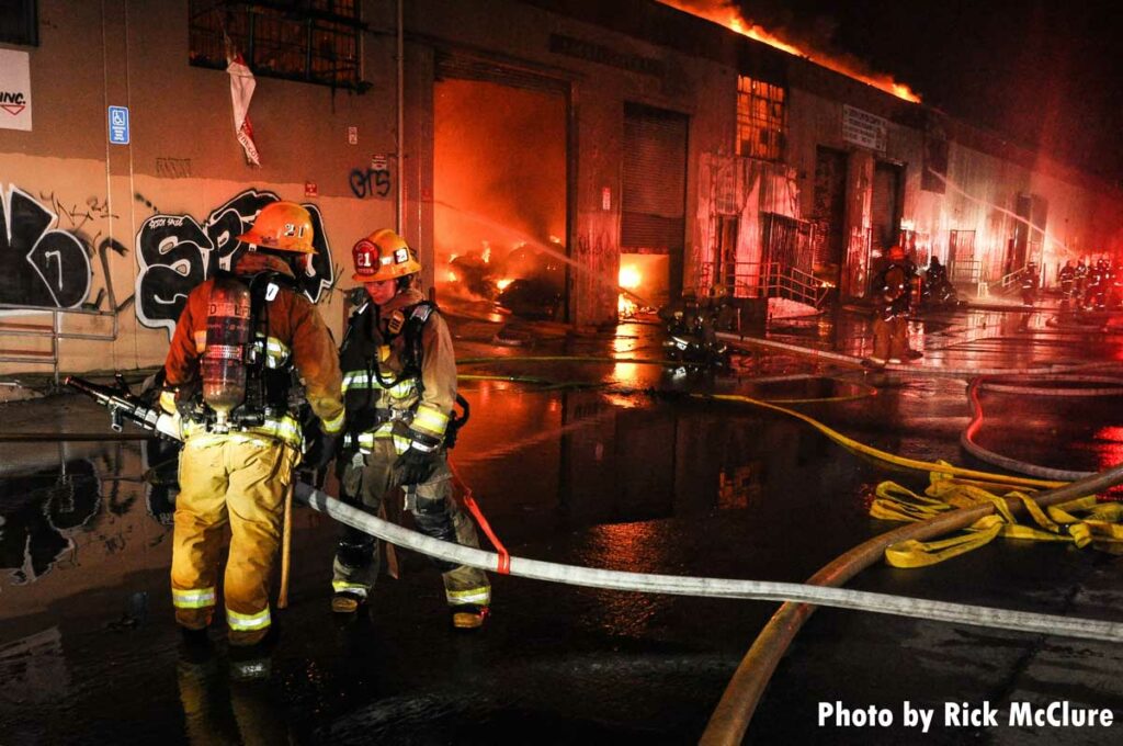 Firefighters with large hoseline attack commercial fire