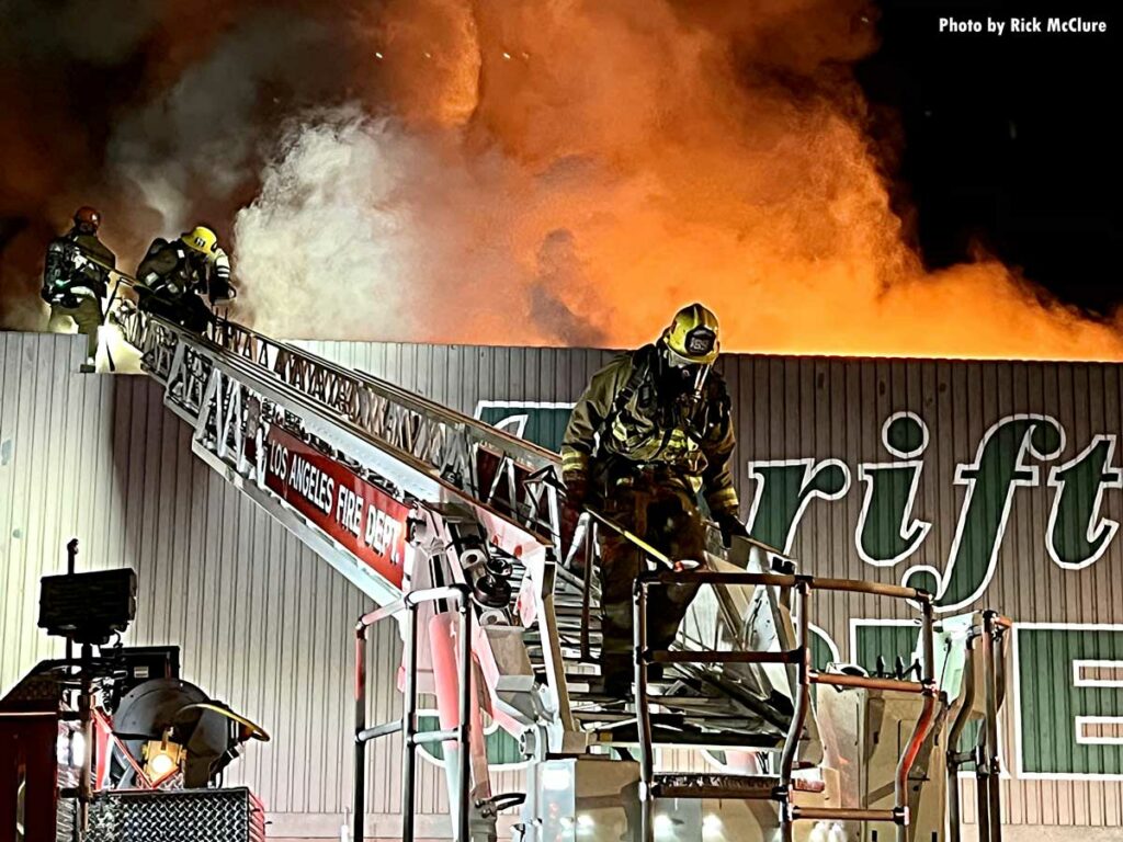 Three Los Angeles firefighters on aerial ladder moving to roof at commercial fire