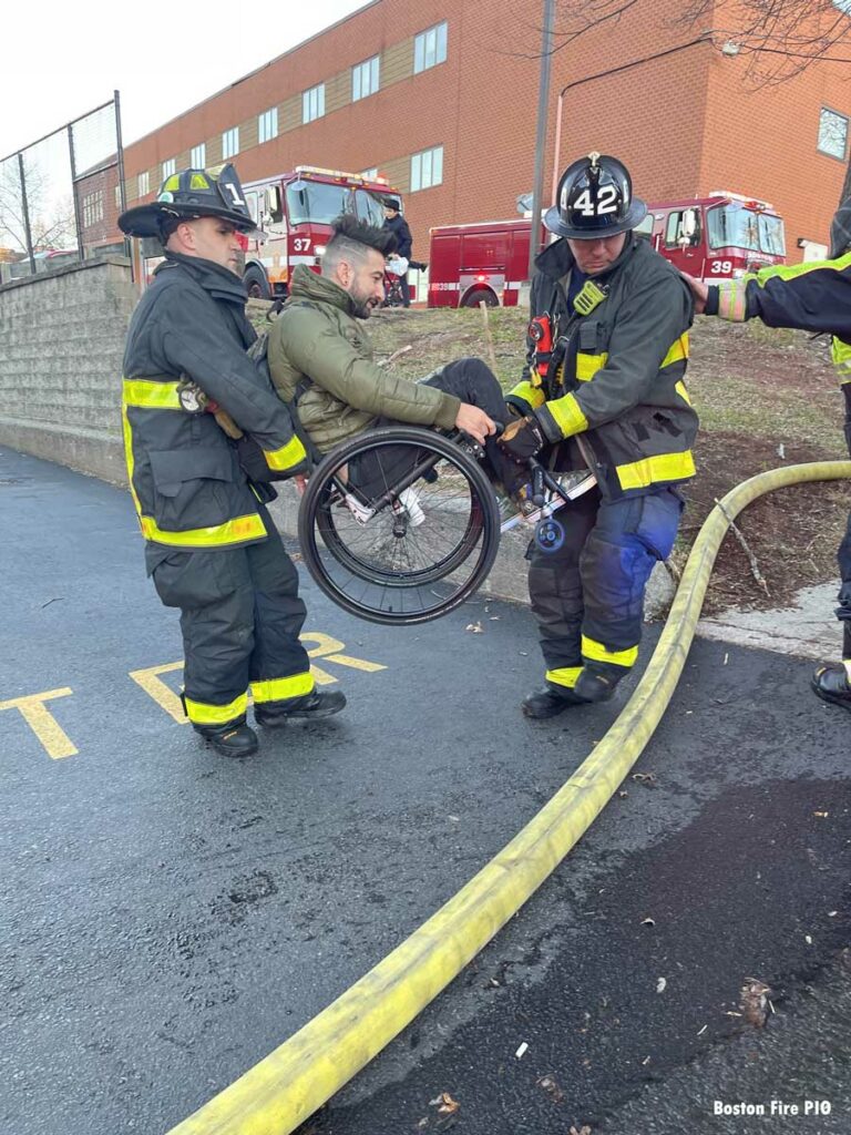 Firefighters lift man in wheelchair over large-diameter hose