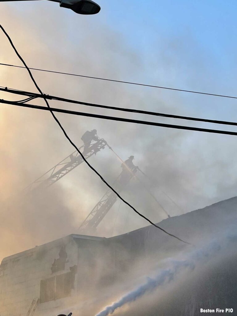 Boston firefighters on aerials with elevated master streams as seen through smoke