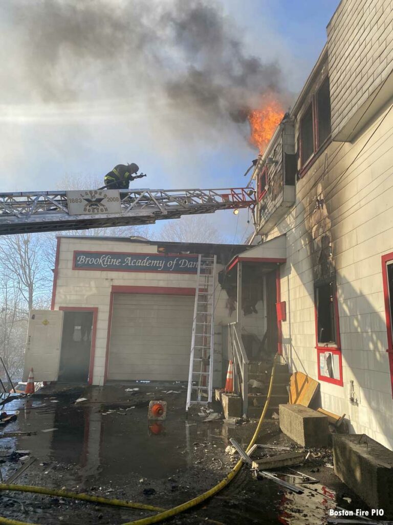 Boston firefighter on aerial ladder with flames on roof