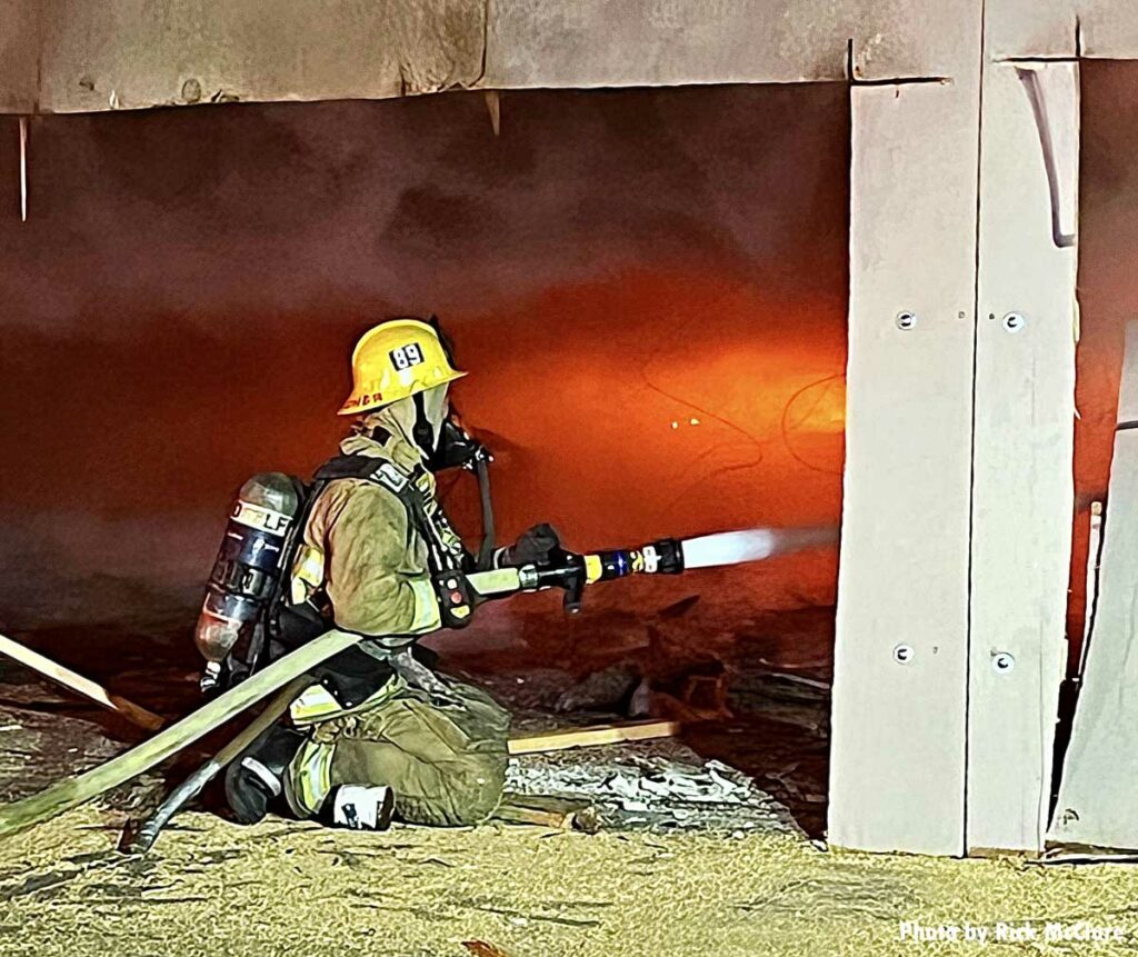 Firefighter in full gear with flames and hoseline