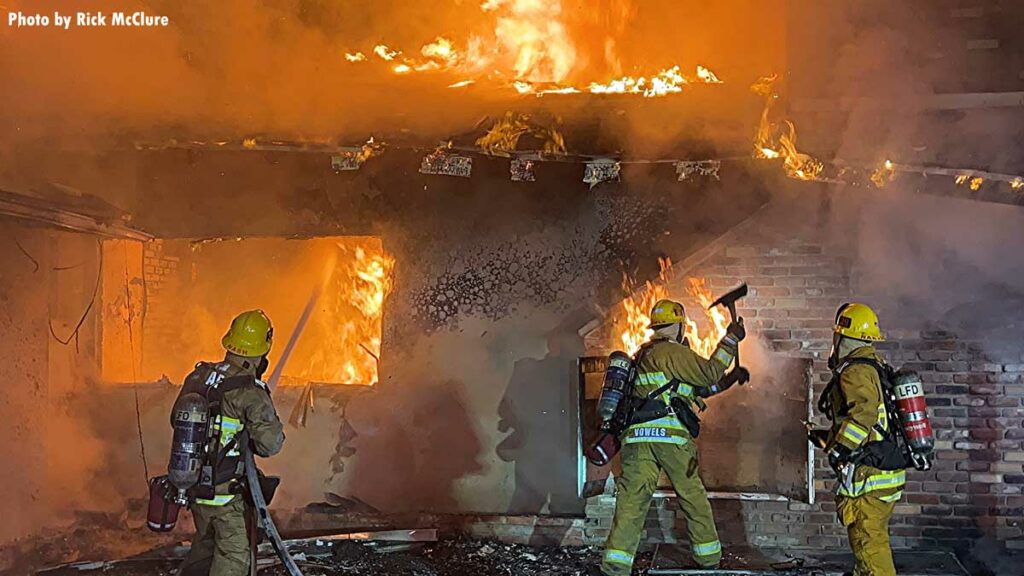 Firefighter swings an ax as another puts water through the window using hose