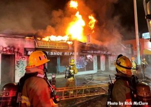 Firefighters with one firefighter putting water on flames shooting through roof