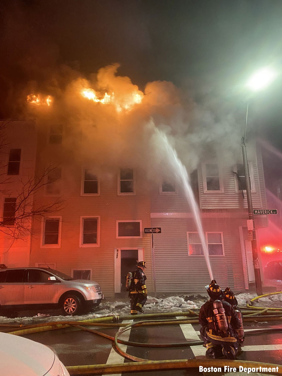 Flames rip along roof with firefighters holding hoseline