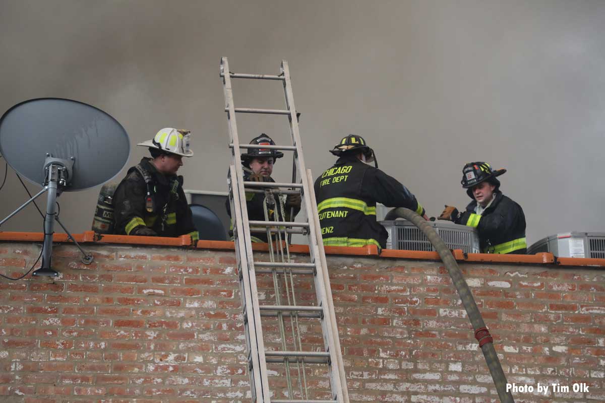 Firefighters with hoseline on roof and ladder