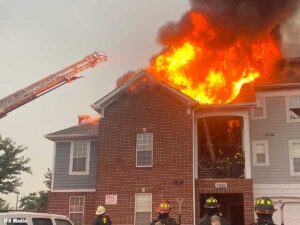 Indianapolis firefighter climbing a ladder while fire burns through a roof